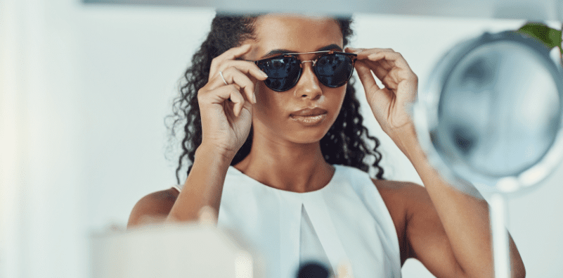 A woman at the eye doctor's office trying on a pair of sunglasses in front of a mirror.